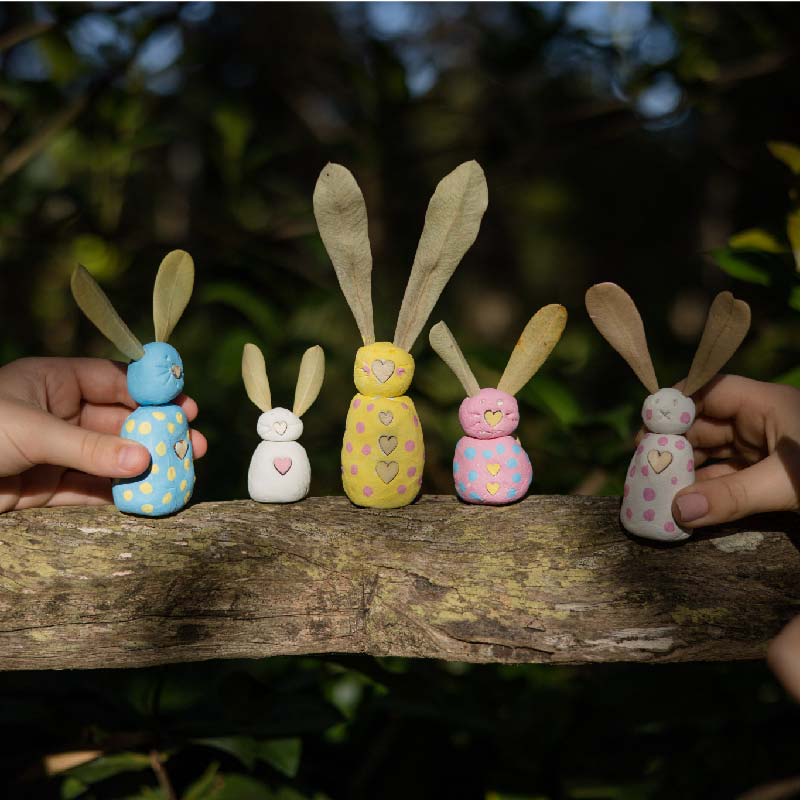 coloured clay bunnies of all sizes on a sunny log in the forest